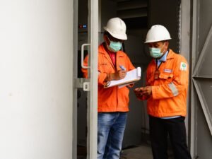 Dua pekerja konstruksi mendiskusikan temuan keselamatan di lokasi kerja