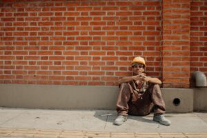 Heat stress management at construction sites: tired construction worker resting against a wall in the sun