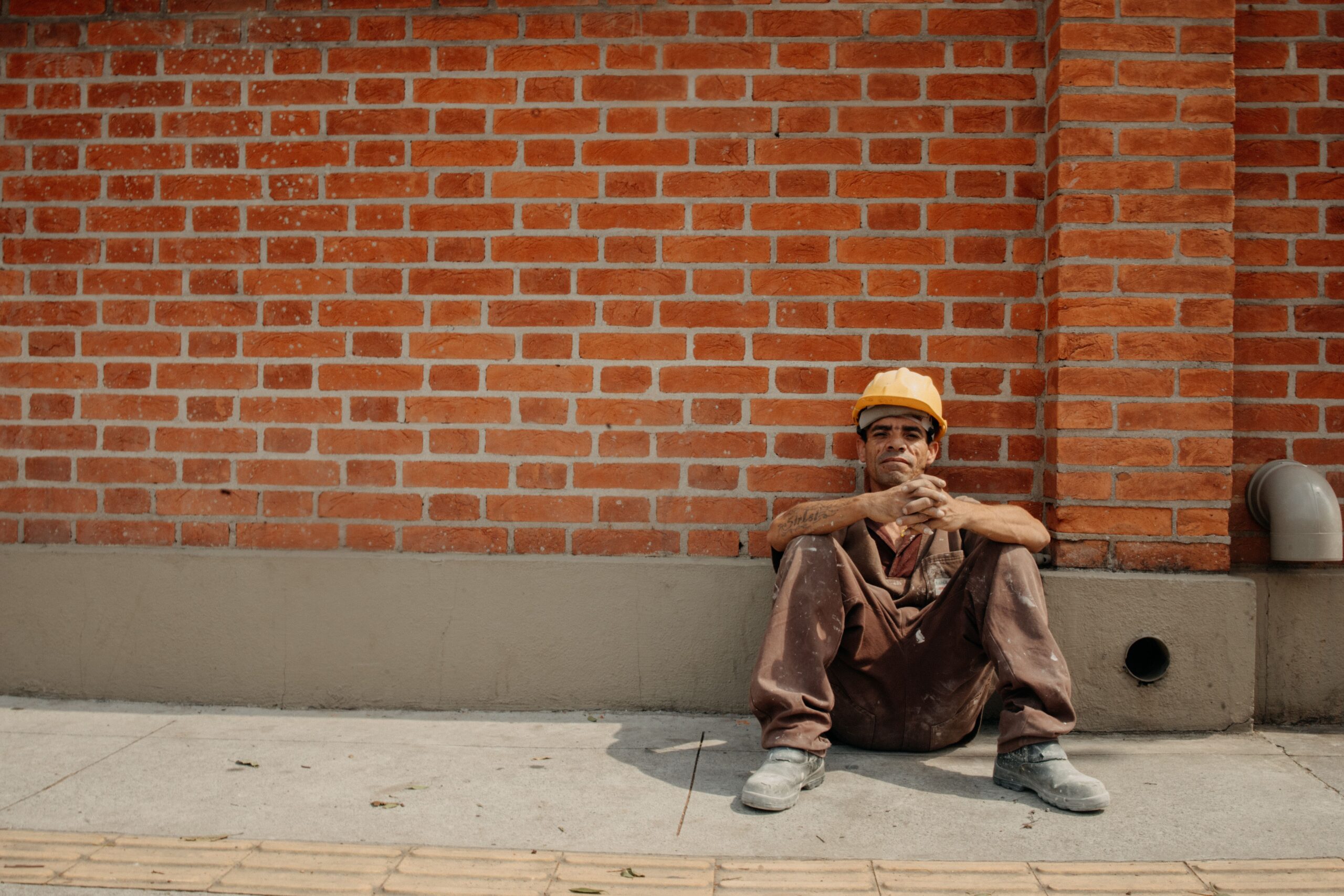 Heat stress management at construction sites: tired construction worker resting against a wall in the sun